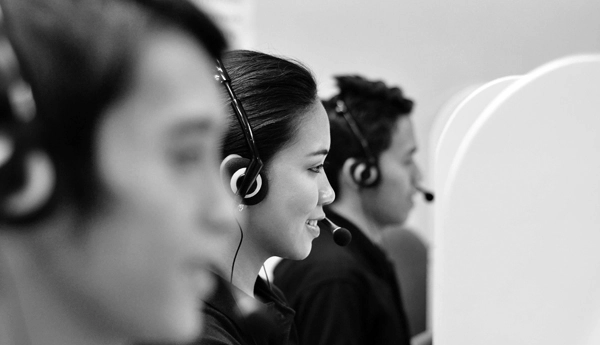 Photo of call center agent with her teammates while talking on a headset.